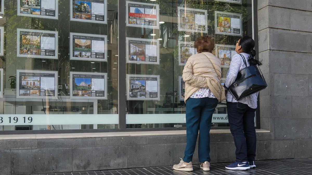 Varias personas miran casas en venta en el escaparate de una inmobiliaria.