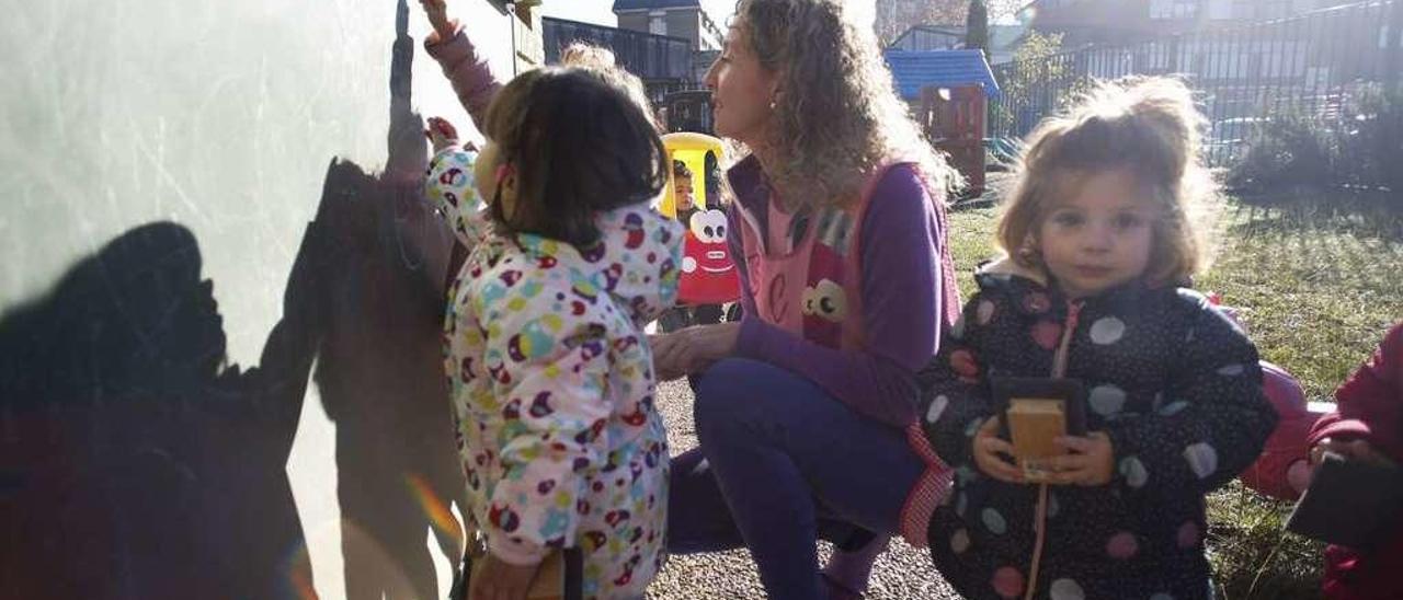 Vera Caballero Lobato escribe en la pizarra junto a la profesora Almudena Álvarez Rodríguez y la niña Lara Colazos Blanco. A la izquierda, Adriana Zaratiegui Calvo, agachada, en el patio de la escuela de La Magdalena.