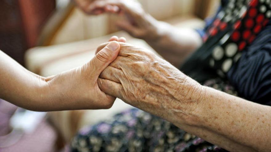 Una mujer sostiene las manos a una anciana.