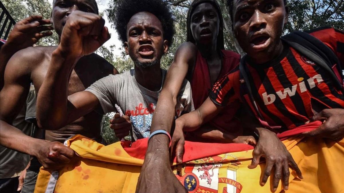 Un grupo de inmigrantes que entraron en Ceuta tras saltar la valla sostienen una bandera española.