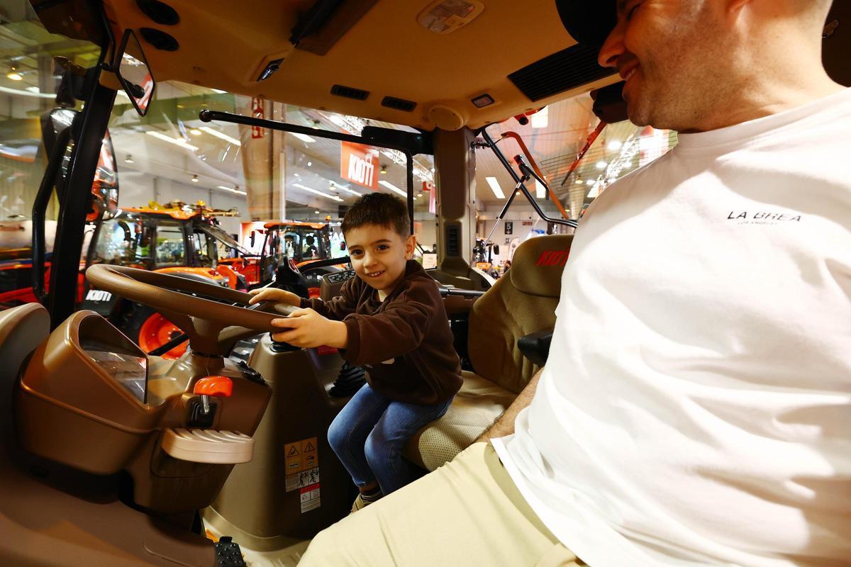 Un joven aficionados a los tractores al volante de un tractor junto a su padre.