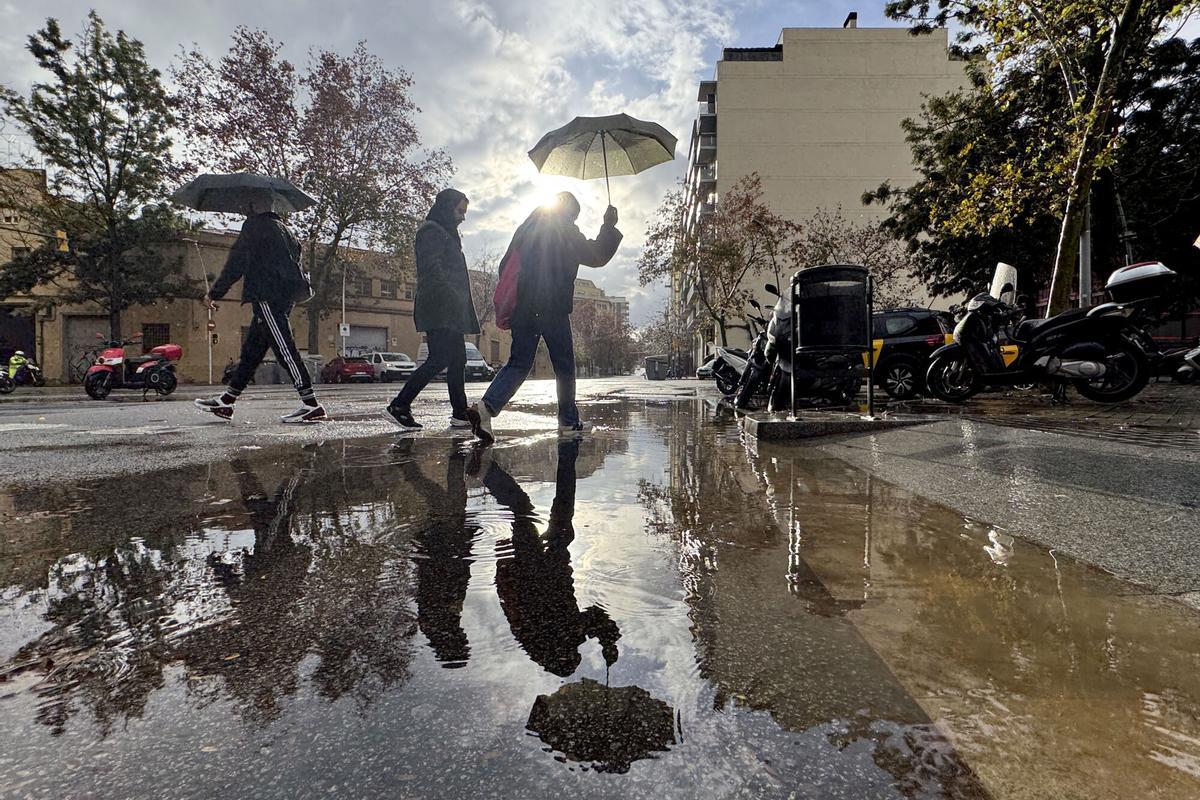 Varias personas cruzan un charco tras una de las intensas tormentas que Barcelona está sufriendo este martes