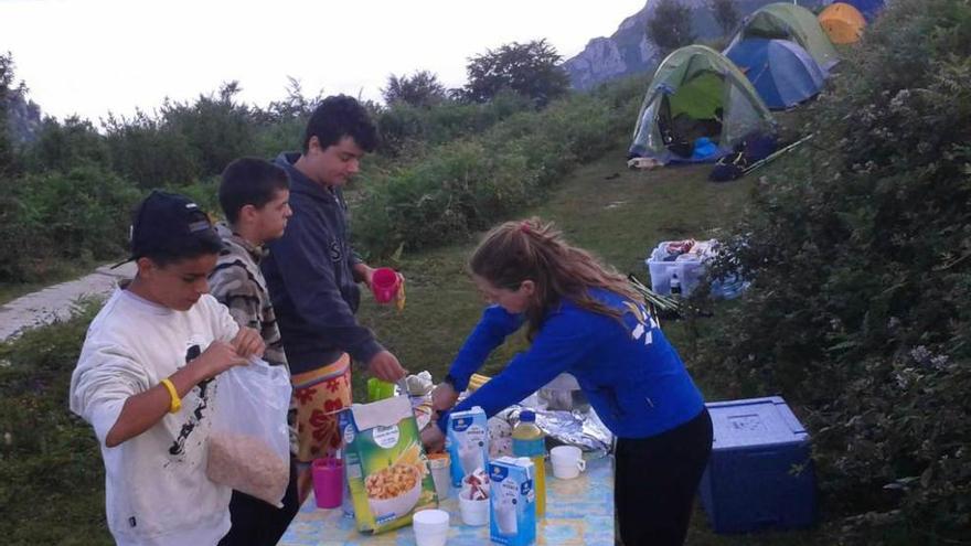 Tres niños y una monitora preparan el desayuno.