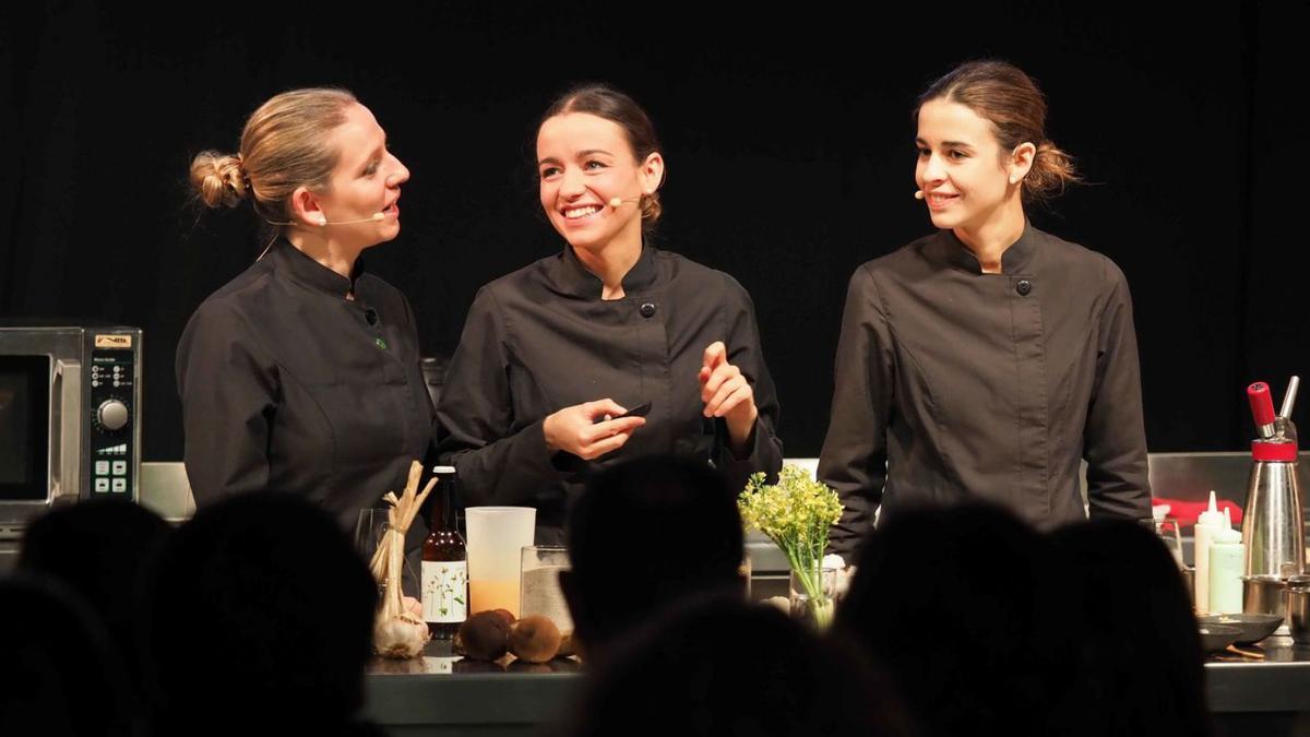 Clara, Martina i Carlota Puigvert del restaurant Les Cols d’Olot, a l’Aula de Cuina de la fira Orígens. A la dreta, diversos visitants gaudint dels productes ofertats. | PERE DURAN/NORD MEDIA