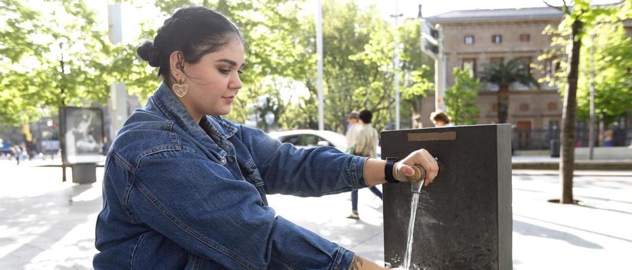 Una chica bebe agua en una fuente del centro de Zaragoza.