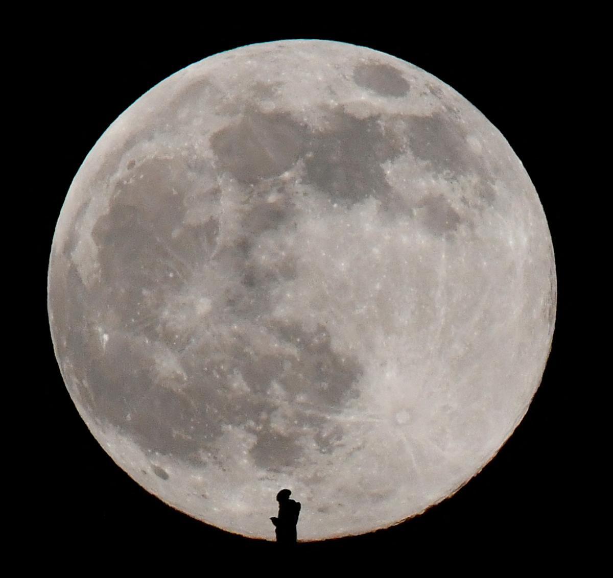 La luna llena se eleva en Glastonbury, Gran Bretaña, tras la silueta de una persona.