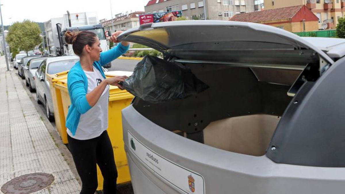 Una mujer tira la basura en un contenedor en Baiona.
