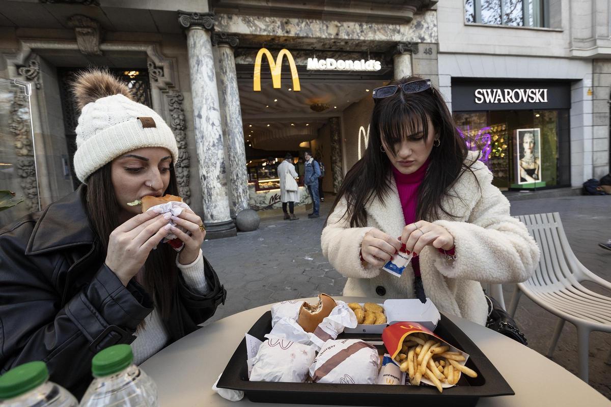 Unas jóvenes comen hamburguesas en la terraza de McDonald's del paseo de Gràcia.