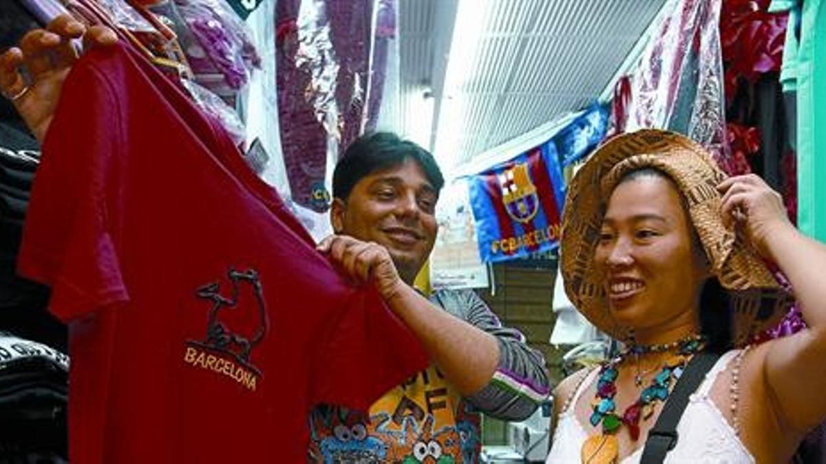 Recuerdo El comerciante indio Ashok Morwani enseña una camiseta a una turista japonesa en su establecimiento de la Rambla de Barcelona.