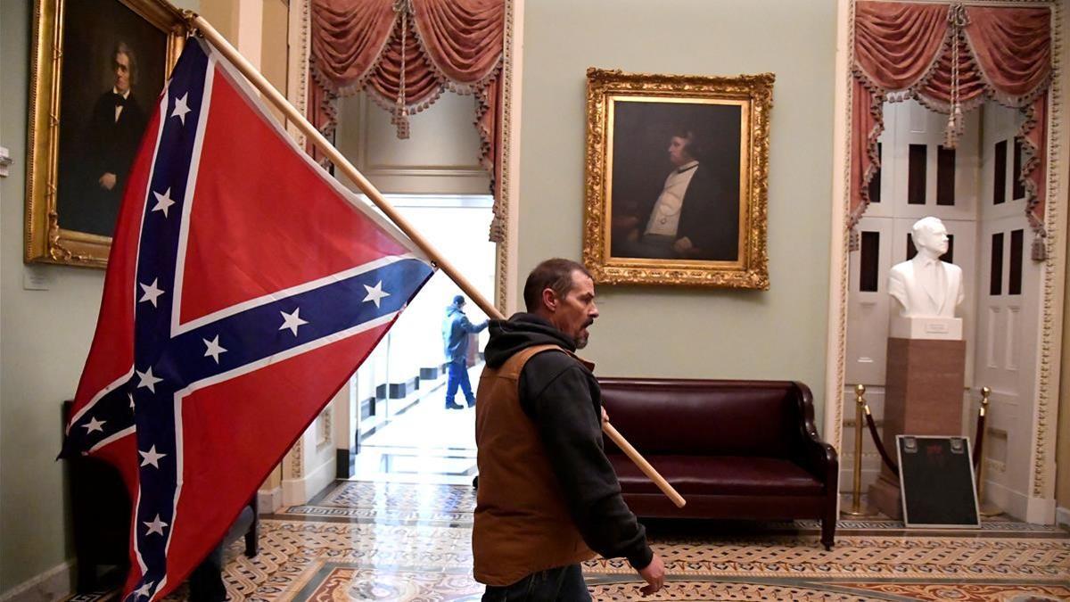 Un participante en el asalto al Capitolio de EEUU pasea por el edificio con una bandera confederada.