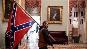 Un participante en el asalto al Capitolio de EEUU pasea por el edificio con una bandera confederada.