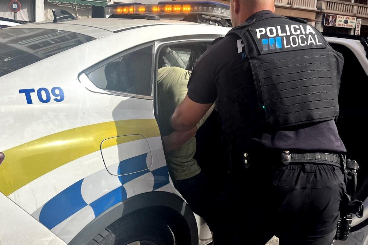 Un policía local mete en el coche patrulla a los asaltantes detenidos.