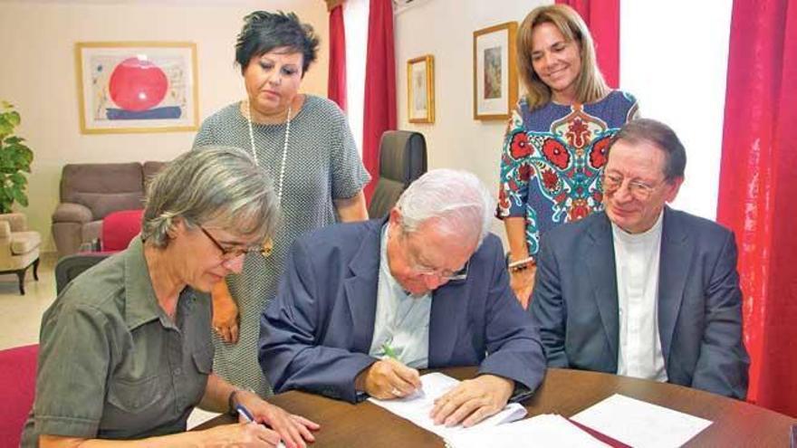 El obispo firma un convenio en presencia de su secretaria, a la derecha.