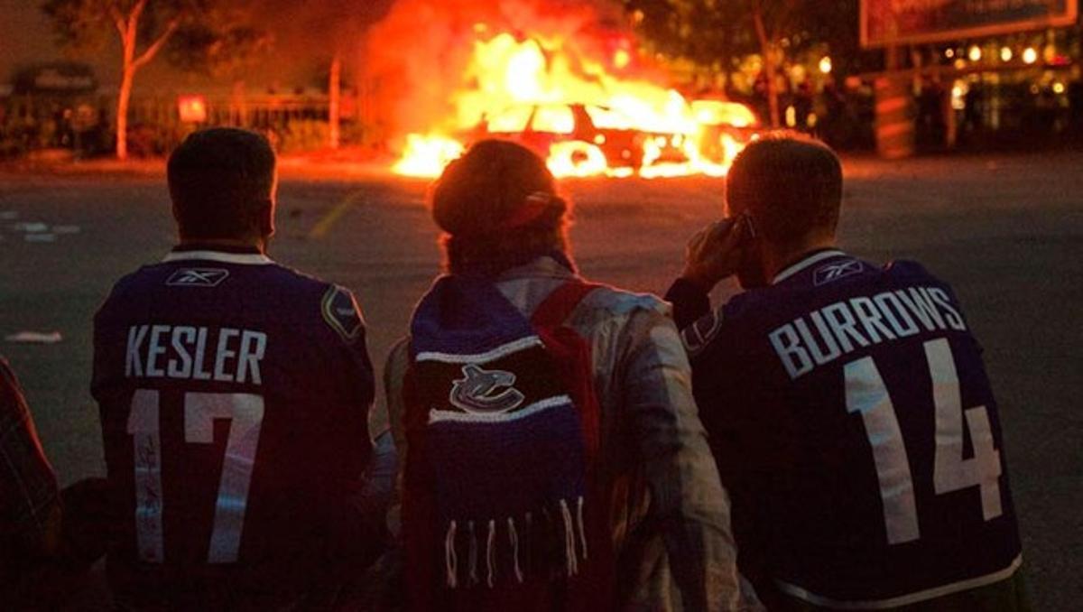 Uns seguidors de l’equip canadenc d’hoquei gel Vancouver Canucks miren un cotxe de policia en flames després dels disturbis de dimecres a la ciutat de Vancouver al perdre l’equip local davant els Boston Bruins, a la final de la Copa Stanley de la NHL.
