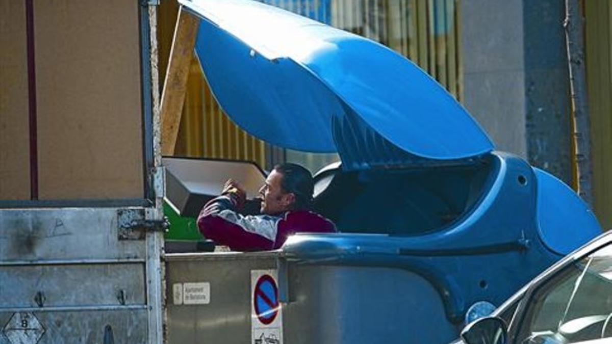 Un hombre saca cajas de cartón de un contenedor de reciclaje del Ayuntamiento de Barcelona, en febrero del 2011.