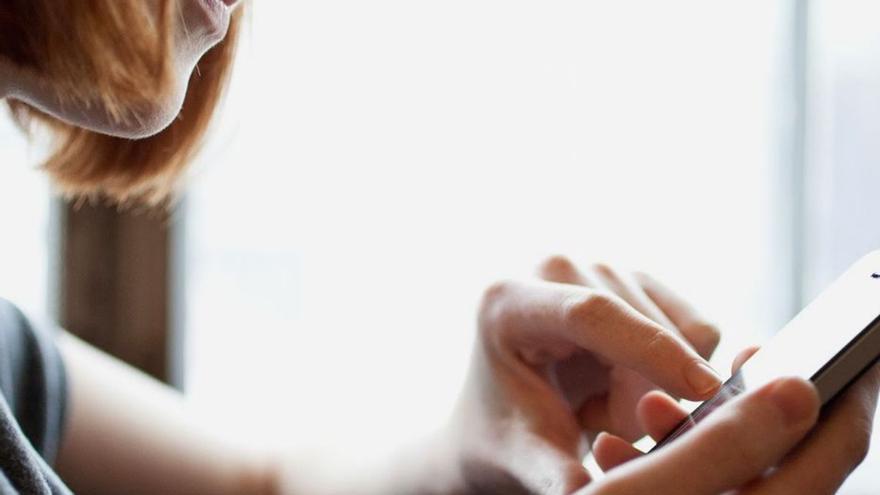 Una mujer lee los mensajes que recibe en su móvil.