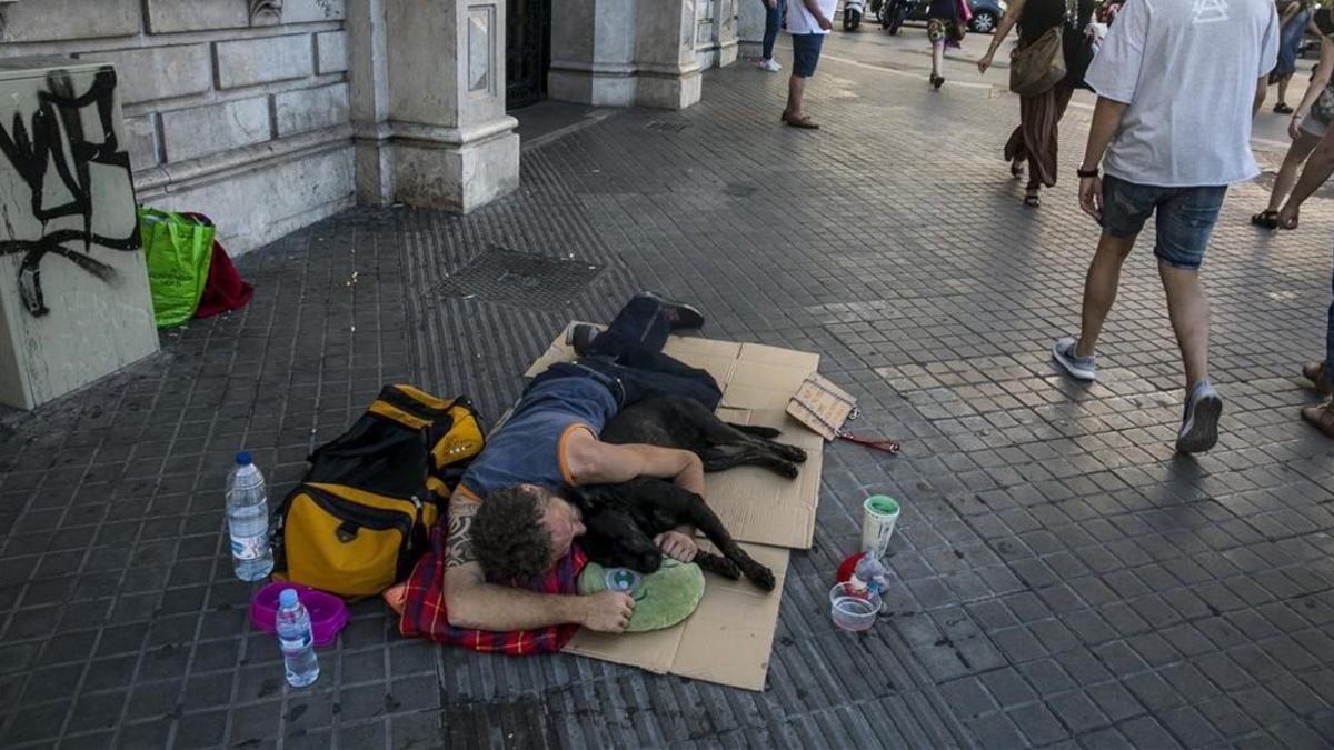 Un sintecho duerme en plena calle en  la Rambla de Catalunya con Plaza de Catalunya