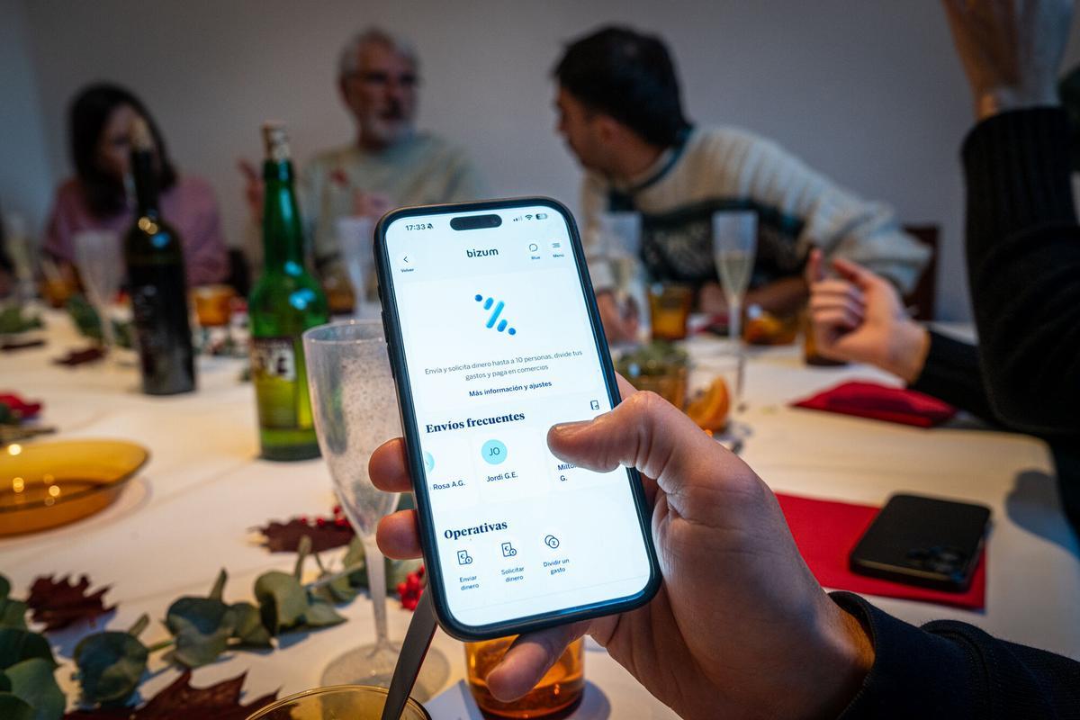 Imagen de archivo de una persona a punto de enviar un bizum, mientras cena con gente. Bizum lo usa hasta el 90% de los jóvenes y supera el 70% en todas las edades