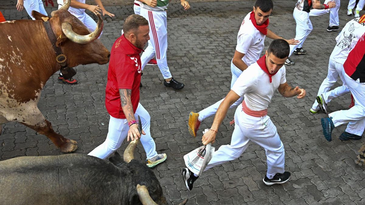 PAMPLONA, 12/07/2025.- Mozos perseguidos por los toros de la ganadería de José Escolar en el sexto encierro de los Sanfermines, este sábado en Pamplona. EFE/Daniel Fernández