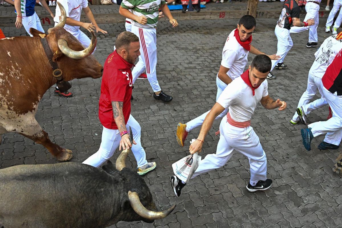 PAMPLONA, 12/07/2025.- Mozos perseguidos por los toros de la ganadería de José Escolar en el sexto encierro de los Sanfermines, este sábado en Pamplona. EFE/Daniel Fernández