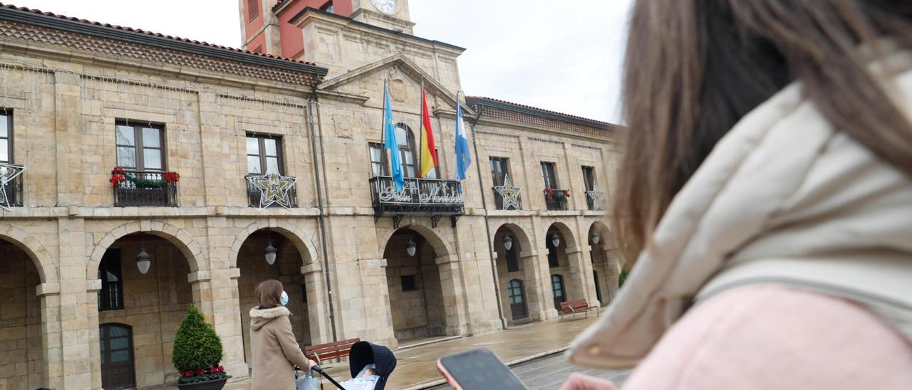 Una avilesina navega con su teléfono móvil ante el Ayuntamiento de Avilés.