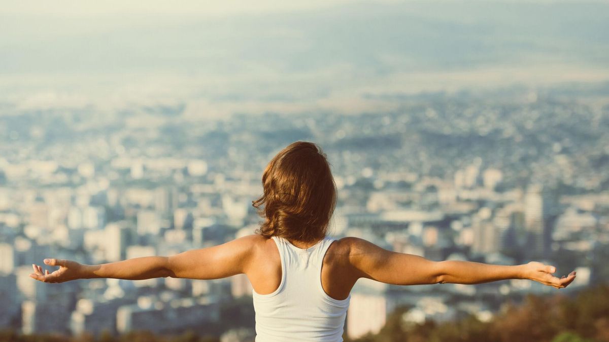 Mujer con los brazos extendidos, de espaldas y, al fondo, una ciudad.