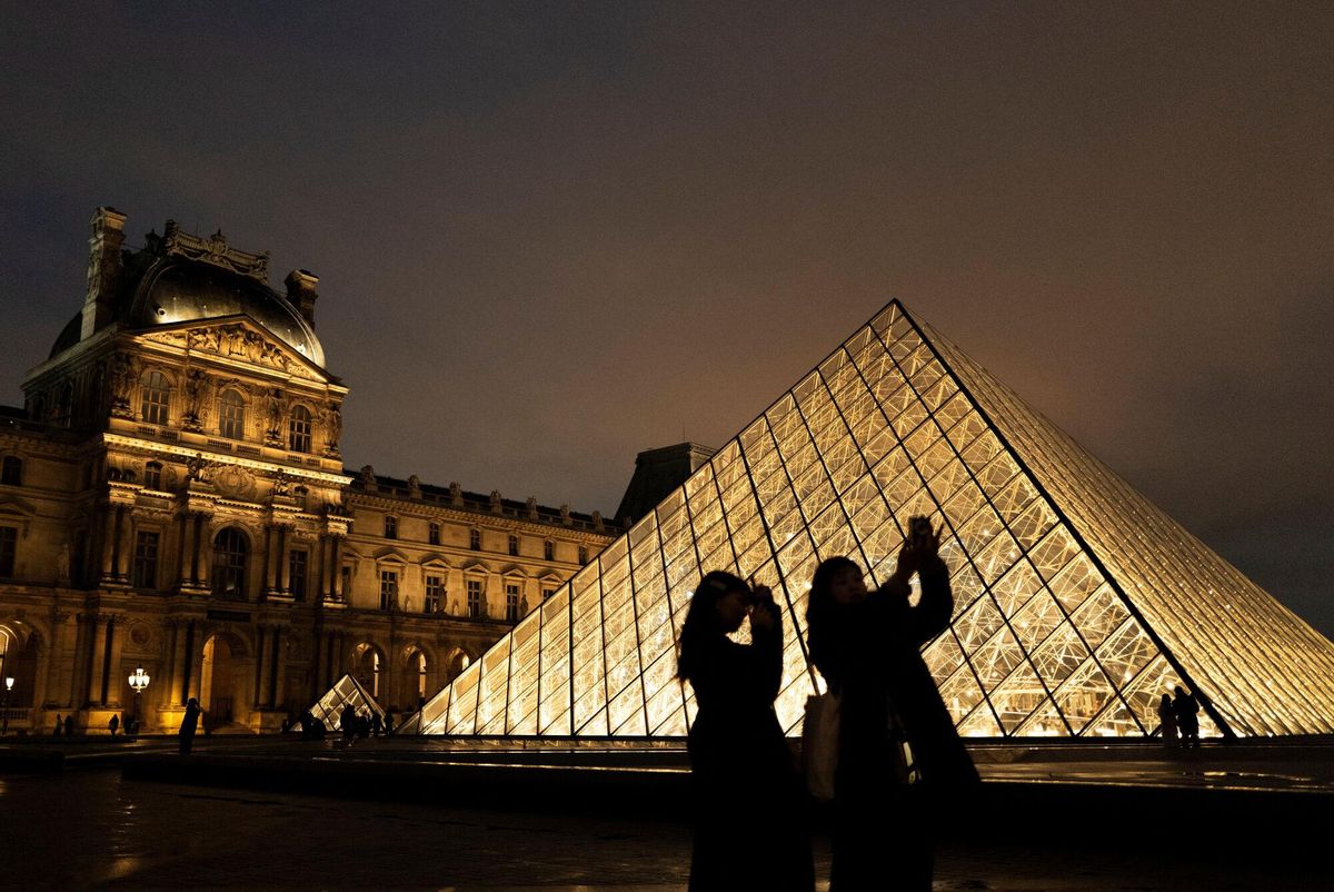 Turistas sacando fotos ante la pirámide de cristal en la entrada del Louvre.