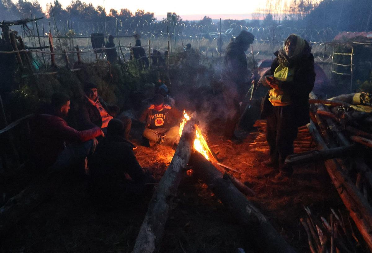 Una fotografía tomada el 10 de noviembre de 2021 muestra a los migrantes calentándose junto a una hoguera en un campamento en la frontera bielorrusa-polaca en la región de Grodno.