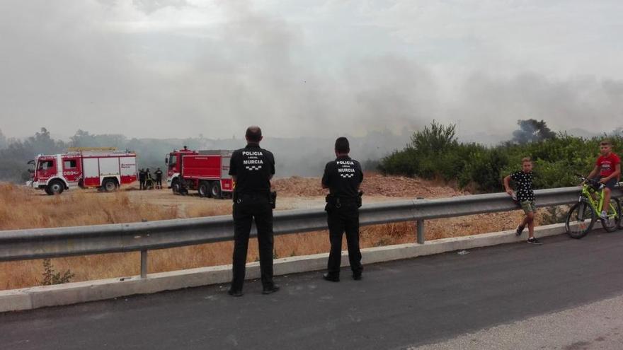 Dos agentes de Policía observan cómo los bomberos extinguen las llamas.