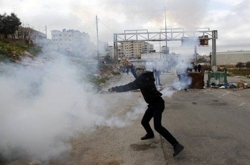 Un palestino devuelve un bote de humo lanzado por las tropas israelíes cerca de la ciudad de Ramallah