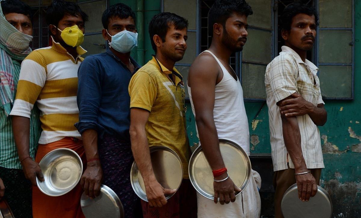 Migrantes con y sin máscaras forman cola para obtener alimentos proporcionados por una oenegé en la ciudad india de Chennai. 