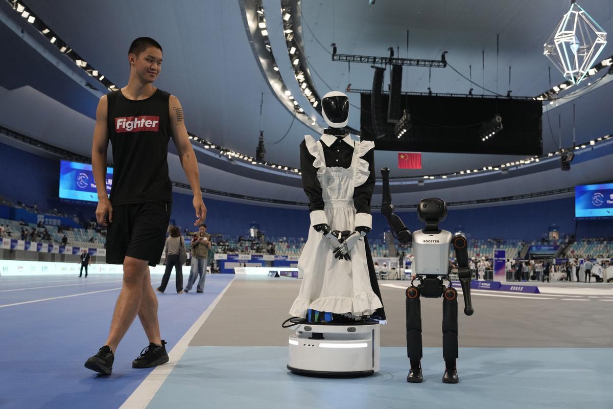 Un hombre camina cerca de los robots en los Juegos Mundiales de Robots Humanoides celebrados en Pekín, China, el viernes 15 de agosto de 2025. (AP Photo/Ng Han Guan)