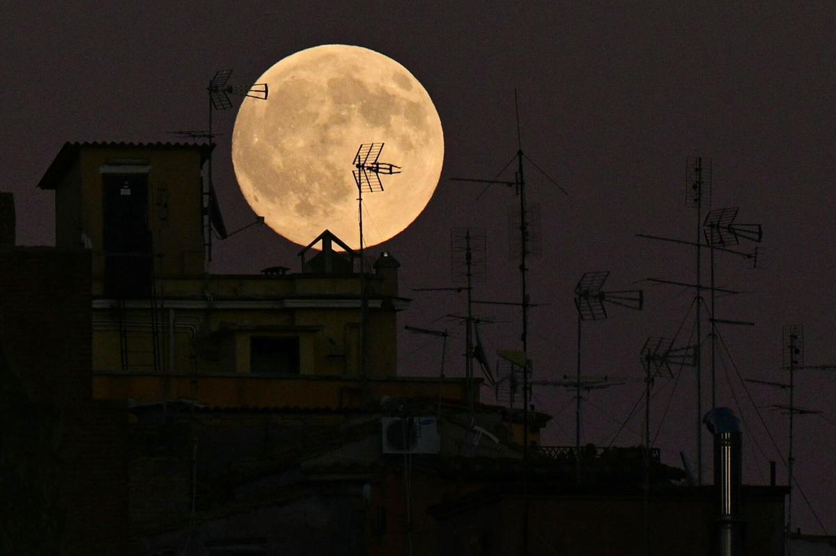 A full moon rises behind old buildings antennas in the historic center of Rome, on October 6, 2025. (Photo by Tiziana FABI / AFP)