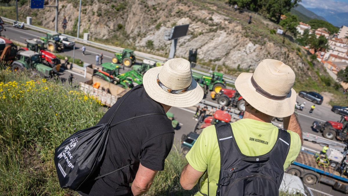 Dos participantes observan desde lo alto la concentración de tractores y agricultores en la AP-7, a la altura del paso fronterizo de El Pertús, este lunes.