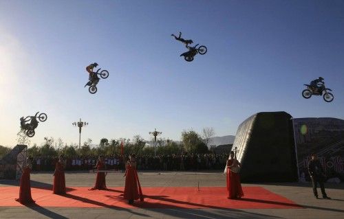 Riders perform stunt jumps on their motorcycles above musicians playing Chinese traditional instruments during the opening ceremony of a forum in Linfen