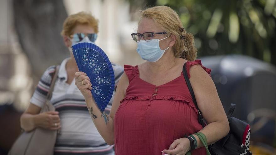 Una señora con mascarilla se abanica por la calle.