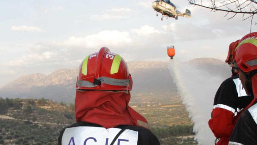 Voluntarios de ACIF y de fondo un helicóptero echando agua sobre la superficie quemada.