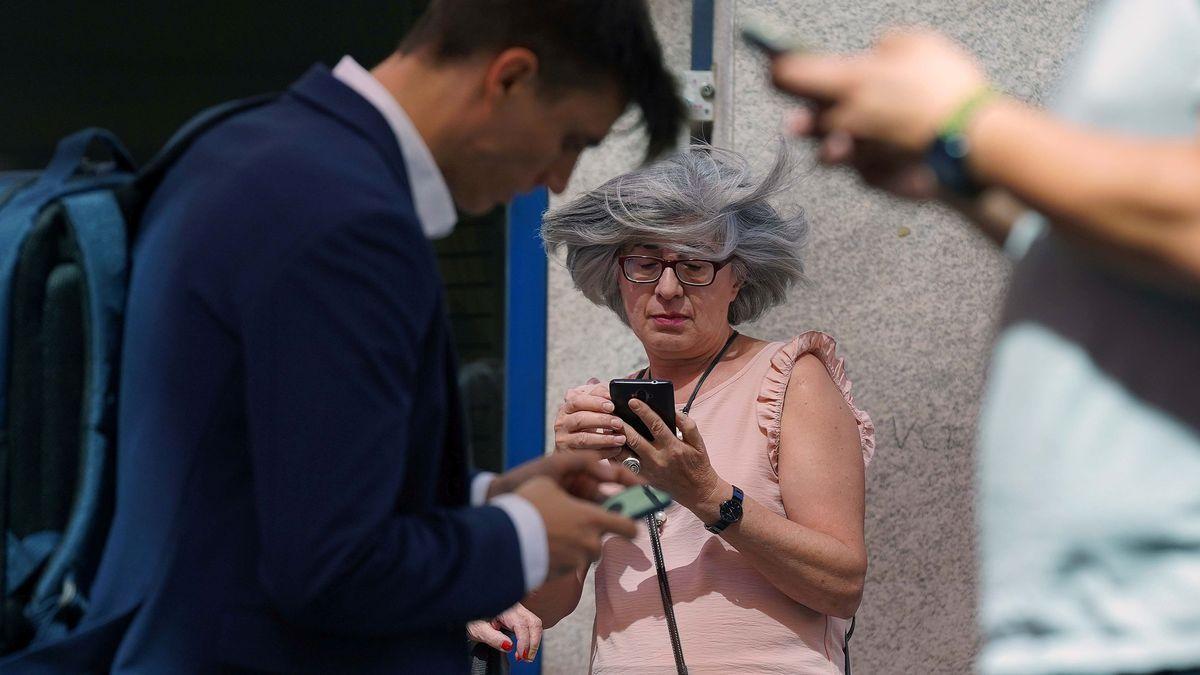 Tres personas miran sus teléfonos móviles en una calle de Madrid.