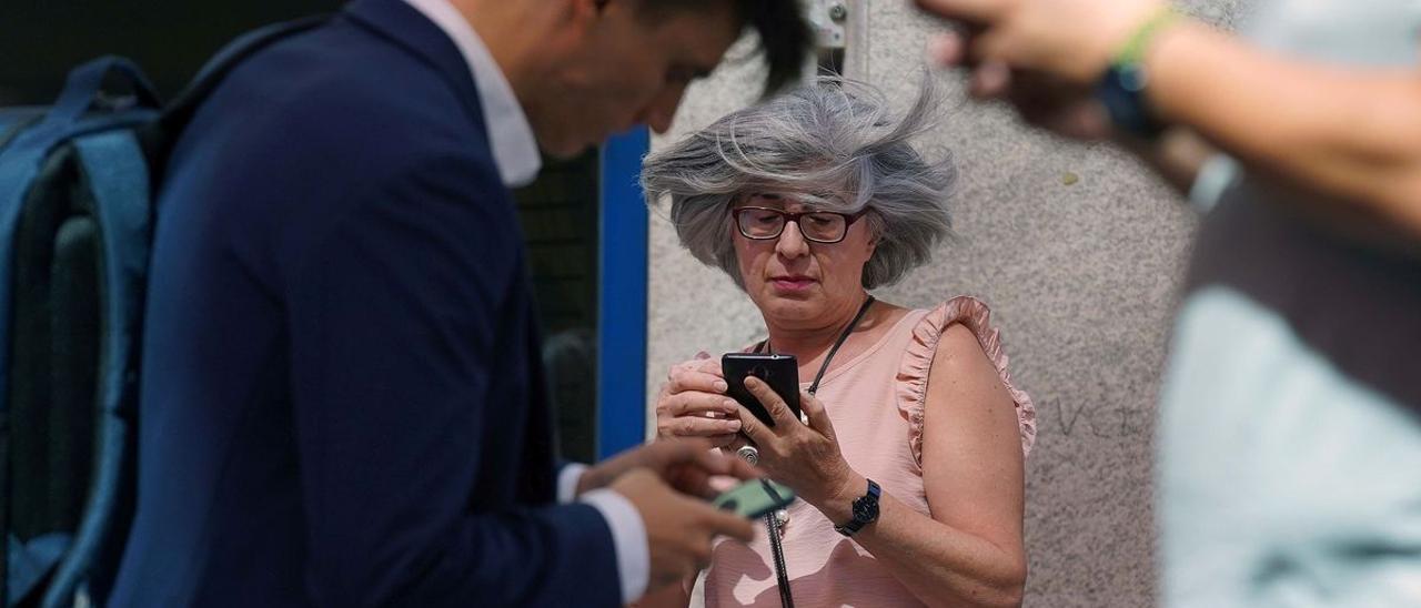 Tres personas miran sus teléfonos móviles en una calle de Madrid.