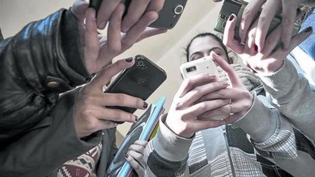 Unos alumnos de secundaria consultan sus móviles a salida de clase.