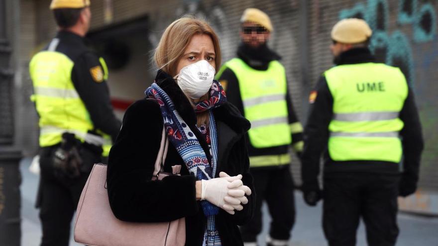 Una mujer camina con una mascarilla junto a miembros de la UME en la calle Carretas en Madrid.