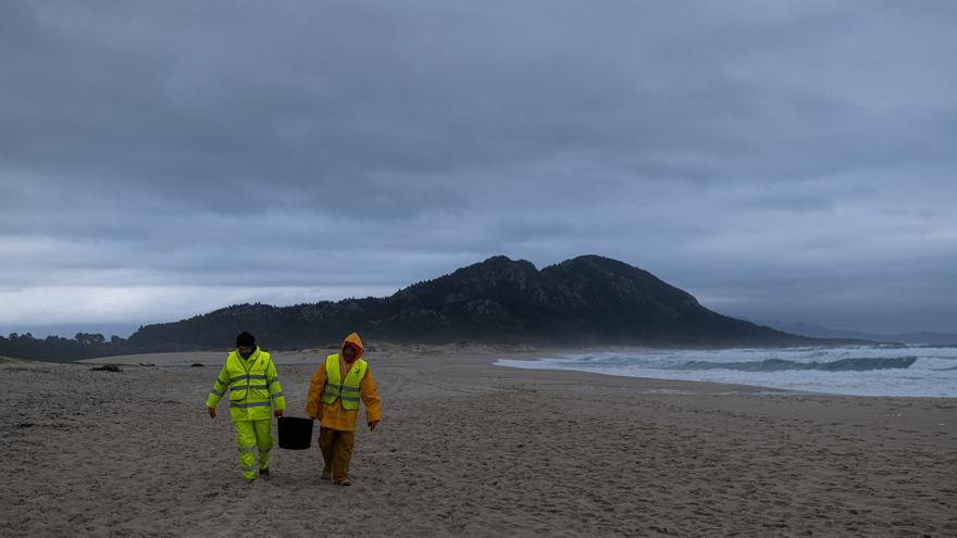 Dos hombres cargan un cubo lleno de pellets, en la playa Area Maior, a 13 de enero de 2024, en Muros, A Coruña, Galicia (España).