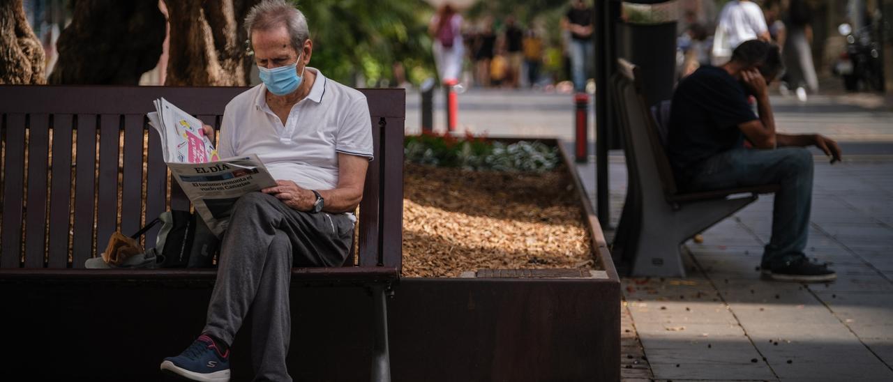 Un hombre con mascarilla lee el periódico en un banco de Santa Cruz de Tenerife.