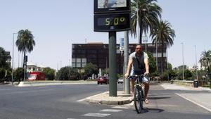 Un joven pasa con su bicicleta junto a un termómetro, expuesto al sol, que marca 50 grados en Córdoba.