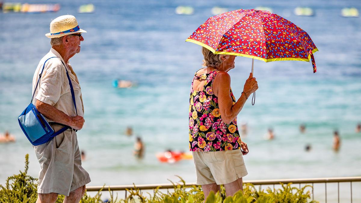 Dos turistas mayores caminan protegidos del sol esta semana en Benidorm.