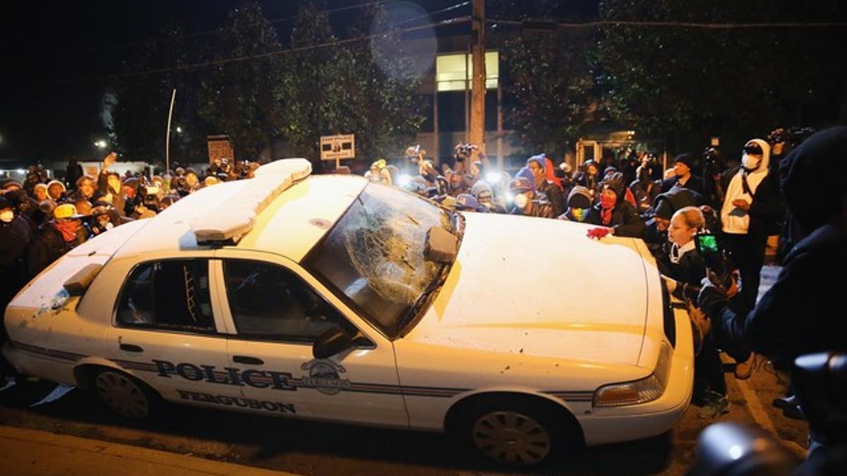 Vecinos de Ferguson golpean un coche de policía, el martes durante las protestas.