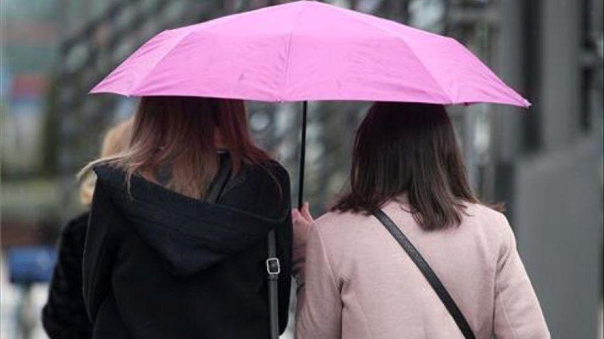 Dos jóvenes se protegen de la luvia con un paraguas.