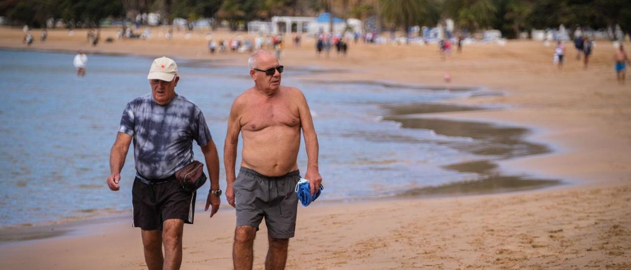 Dos hombres pasean por la orilla de la playa de Las Teresitas.