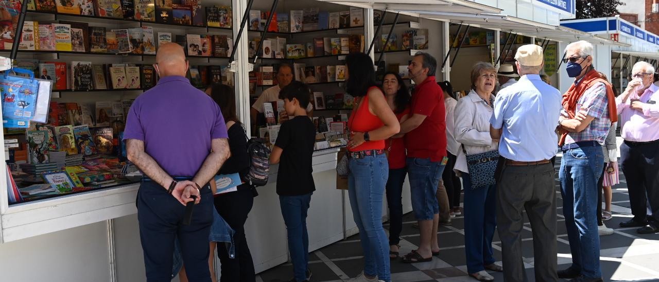 Varios lectores, entre ellos un adolescente, observando los libros de una caseta de la Feria del Libro de Badajoz.