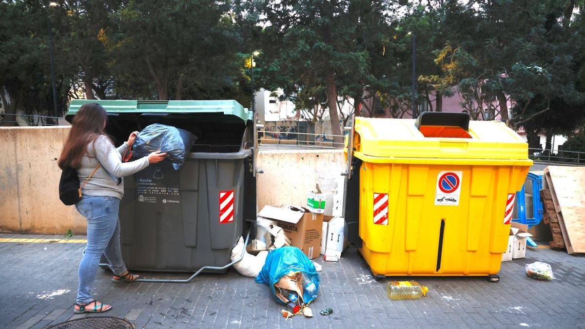 Una mujer deposita una bolsa de basura en un contenedor.